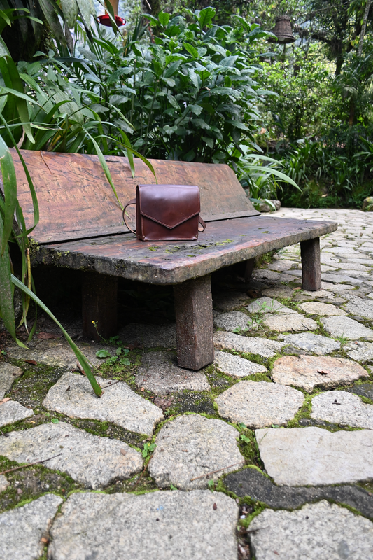 Mahogany crossbody fanny pack pictured on a wooden bench in Peru. 